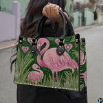 Front view of flamingo handbag displaying pink flamingos and tall green tropical foliage.