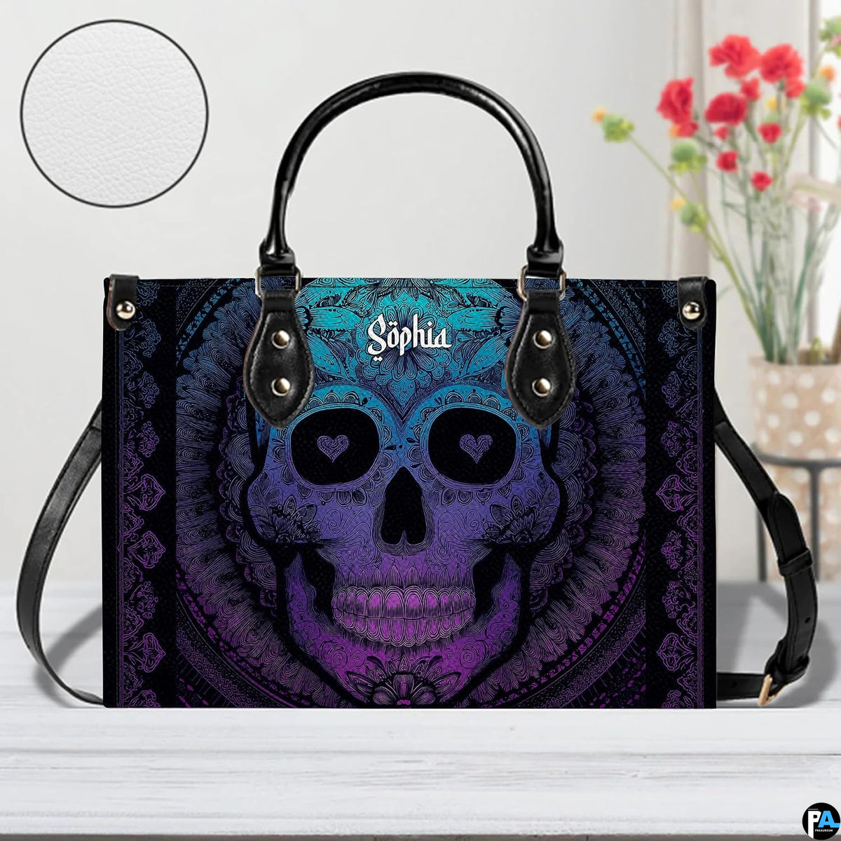 Sugar skull handbag on white table beside floral bouquet with texture swatch inset.