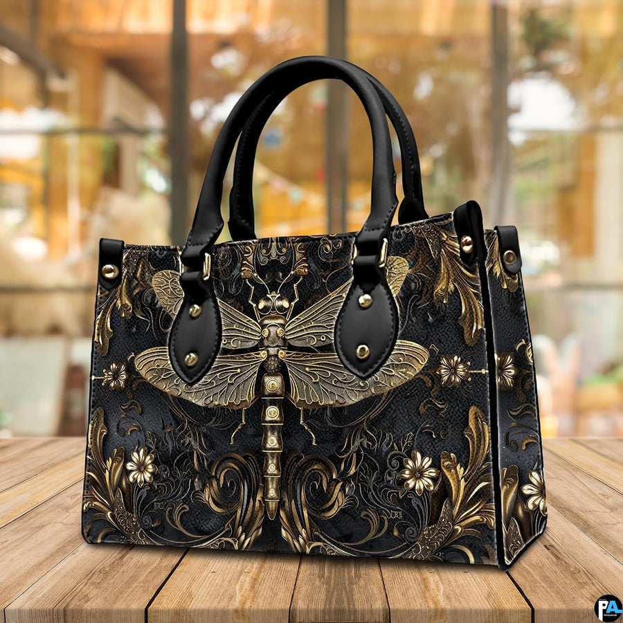 Angled perspective view of gold dragonfly handbag resting on a rustic wooden tabletop near a window