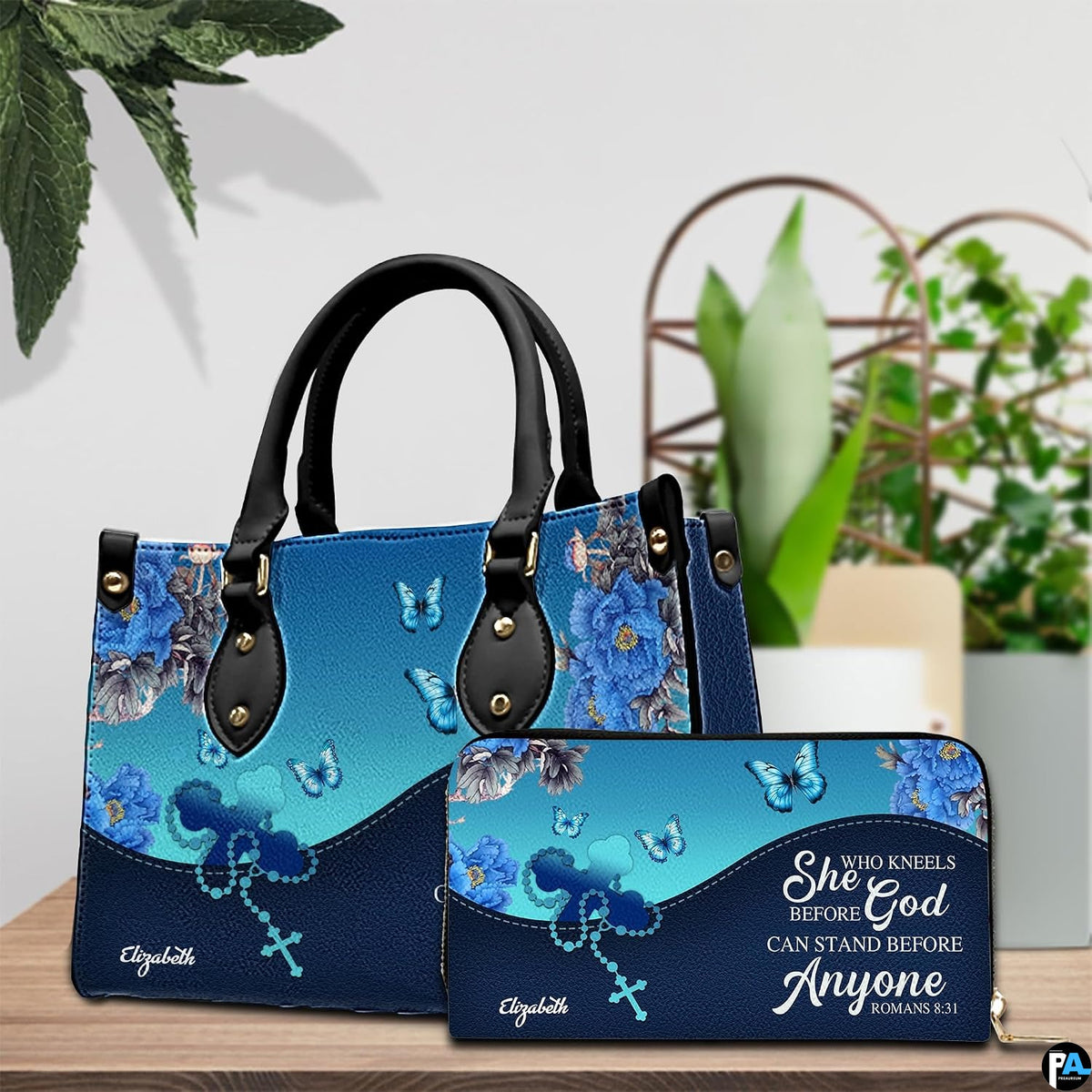 Handheld item and companion accessory with blue peony and rosary art placed together on wooden table near potted plant.