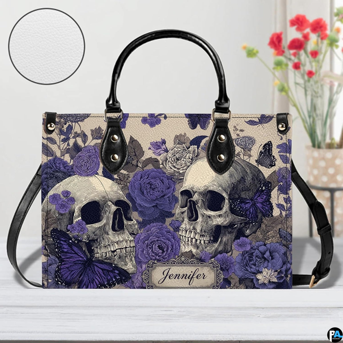 Violet skull handbag on white wooden table beside floral vase with texture swatch inset.