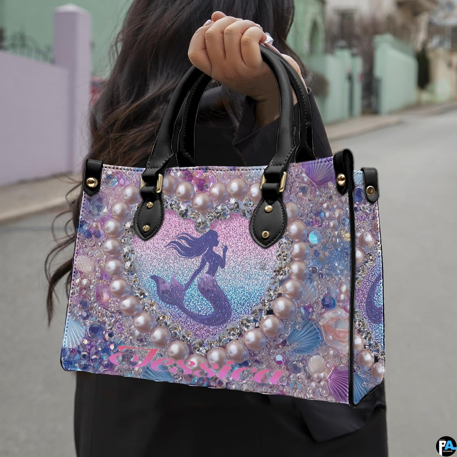 Side profile of mermaid handbag showing structured silhouette and black carrying handles.