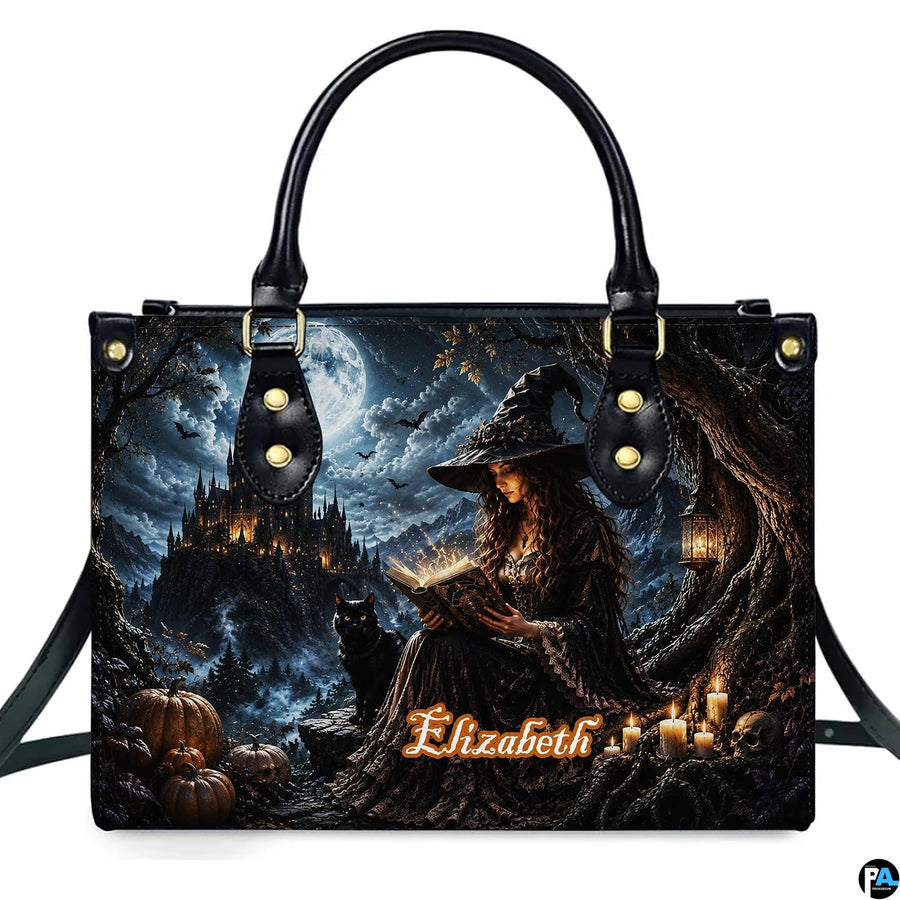 Gothic witch satchel showing seated sorceress reading glowing spellbook with black cat and cliffside castle under full moon.