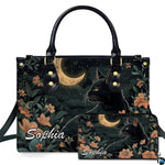 Black cat profile looking toward a golden crescent moon amid peach floral blooms.