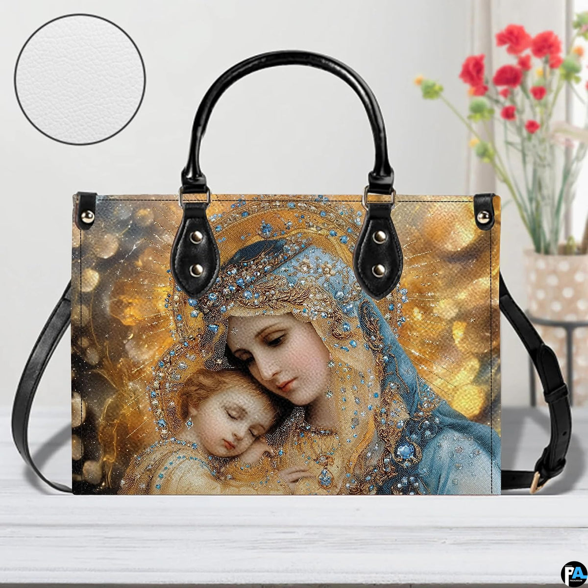 Virgin Mary and infant Jesus handbag displayed on white wooden table beside fresh floral bouquet